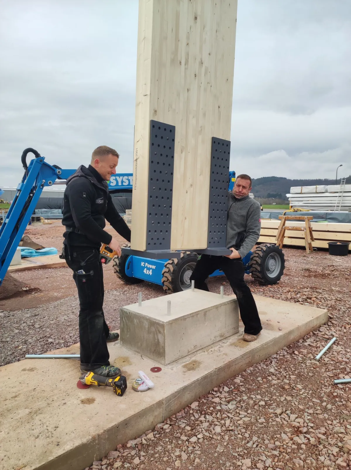Zwei Monteure von Holzbau Dawen richten eine Holzstütze mit Stahlfuß auf dem Punktfundament aus