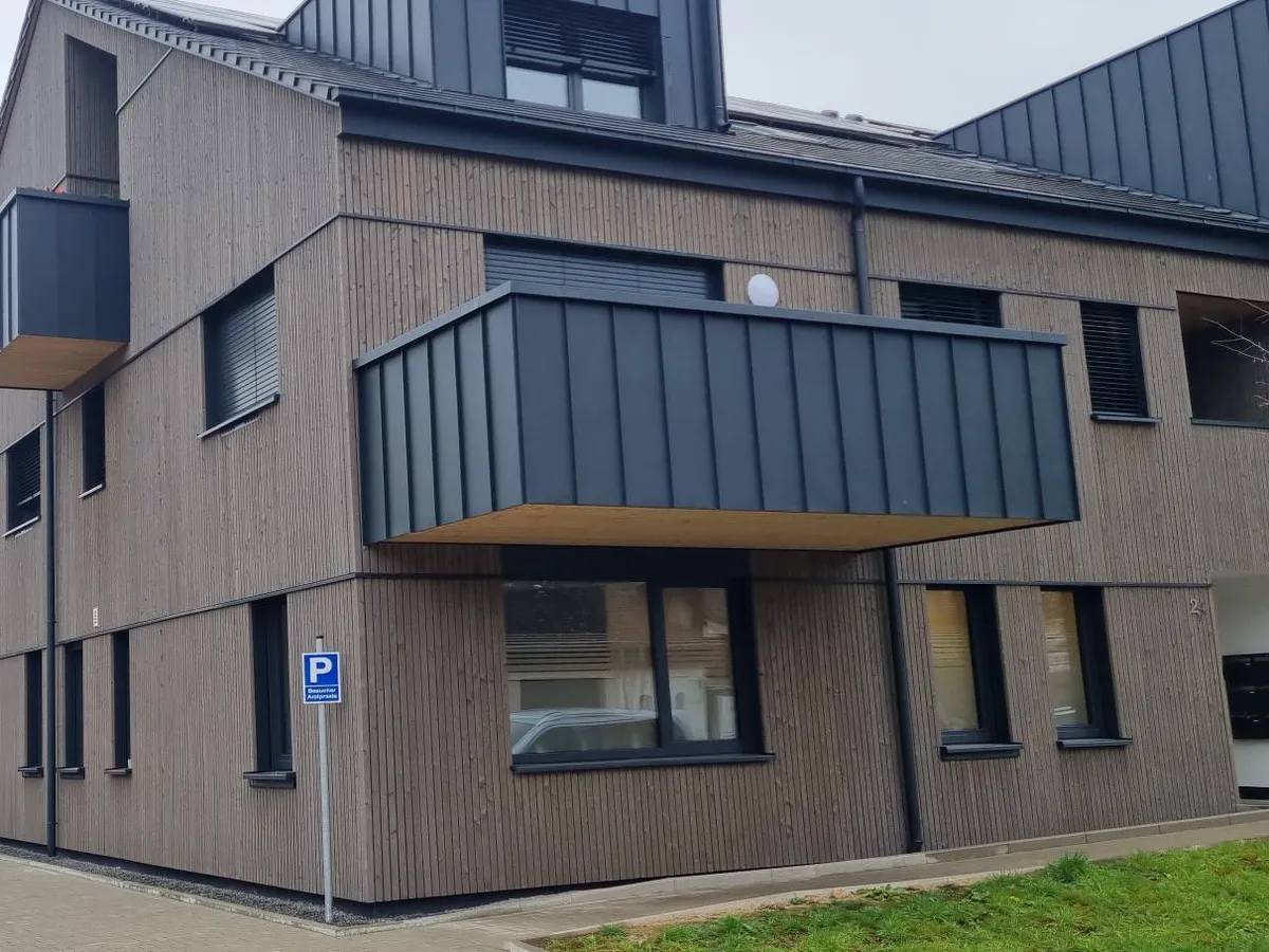 Gebäudeecke des Ärztehauses in Tawern mit Holzfassade und dunklen Balkonen, Detailansicht